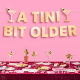 A Tini Bit Older Gold Foil Banner - 5 Ft. | Martini Decoration, Birthday Party Sign, Casino Decor, Girl Cocktail Backdrop, Vegas Photo Booth Background